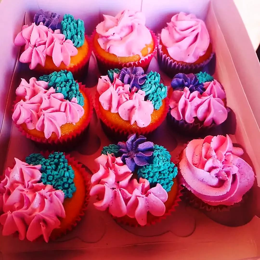 Doce cupcakes decorados con frosting rosa, azul y morado en caja