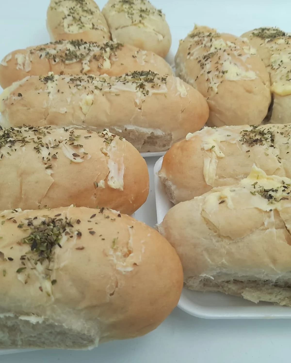 Bandeja con panes de ajo artesanales sobre platos blancos, untados con manteca, perejil y oregano, recien horneados por 2M Reposteria en San Lorenzo